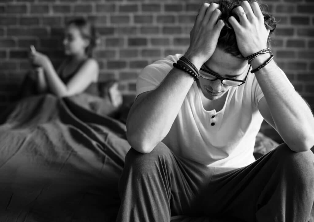 Man feeling stressed after losing an erection while his partner sits in the background